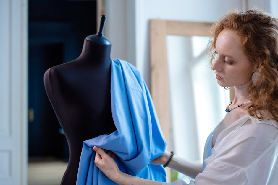 Female fashion designer draping blue fabric on a black mannequin indoors.